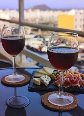 Two wine glasses on a table with a cheese and meat board, set against a cityscape view. - Dream in Paradise - Ocean Views & AC (Corralejo)