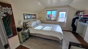 Ein Schlafzimmer mit Bett, Nachttisch, Lampe, Spiegel, Fenster und Kleiderschrank.