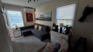 Ein modernes Wohnzimmer mit grauem Sofa, einem gemusterten Teppich und einem Fenster mit Jalousien.
