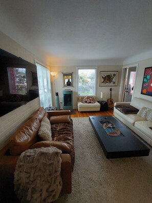 A living room with a brown leather sofa, a white couch, a coffee table, and a fireplace. - Family Cottage-House in Scenic James Bay, Victoria: 1 Blk to Ocean & Ogden Pt! (Victoria)