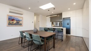 A modern kitchen with white cabinets, a blue refrigerator, and a dining area with a wooden table and green chairs. - Elmrise in Elsternwick (Saint Kilda East)