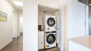 A laundry room with two stacked front-loading washing machines, a small sink, and a door leading to another room. - Elmrise in Elsternwick (Saint Kilda East)