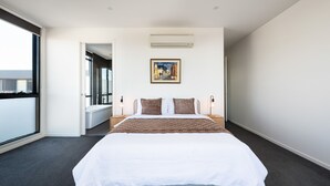 A hotel room with a large bed, a painting on the wall, and a view through an open door. - Elmrise in Elsternwick (Saint Kilda East)