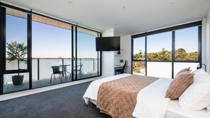 A bedroom with a large bed, a TV mounted on the wall, and a balcony with a table and chairs. - Elmrise in Elsternwick (Saint Kilda East)