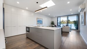 A modern kitchen with a central island, white cabinetry, and a large window offering a view of the outdoors. - Elmrise in Elsternwick (Saint Kilda East)
