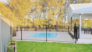 Ein Garten mit Schwimmbad, umzäunter Fläche und überdachter Terrasse.