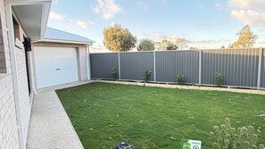 A residential backyard with a well-maintained lawn, a garage, and a tall fence. - The Silverwoods Retreat (Yarrawonga)