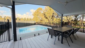 Ett takförsett utomhusområde med en pool, ett bord med stolar och utsikt över träd.