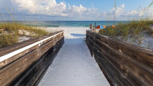 Un sentier en bois mène à une plage d’où l’on a une vue dégagée sur l’océan et où sont installés des parasols de plage.