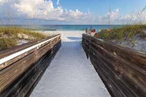 Ein Holzsteg führt zu einem Strand mit freiem Blick auf das Meer und Strandsonnenschirmen.