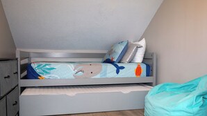 Un lit superposé avec une étagère inférieure, un pouf vert turquoise et une étagère fixée au mur.