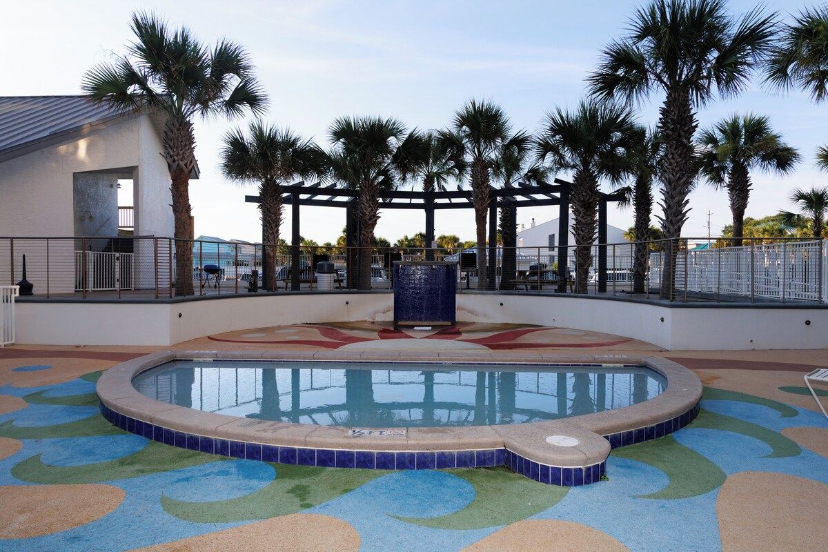 A swimming pool with a tiled deck, surrounded by palm trees and a covered area with a pergola.