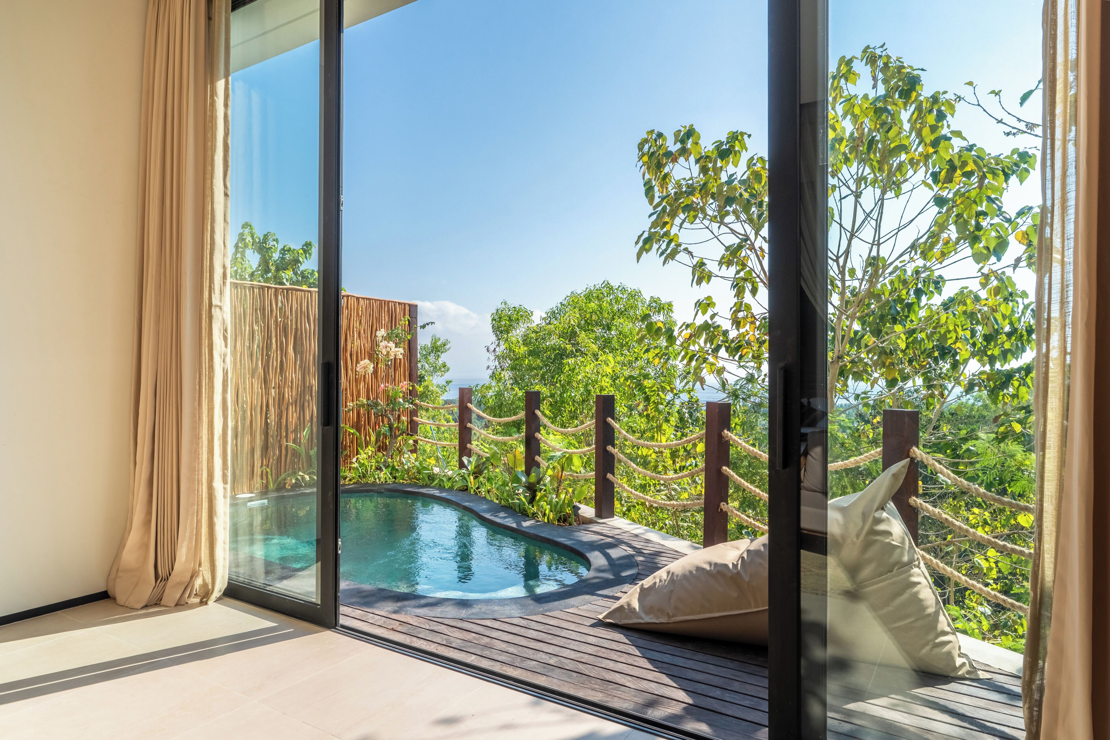 Un balcón con piscina, terraza de madera y vistas a árboles.