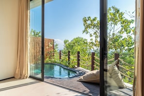 A balcony with a pool, wooden deck, and a view of trees. - Villa Karilla (Penida Island)