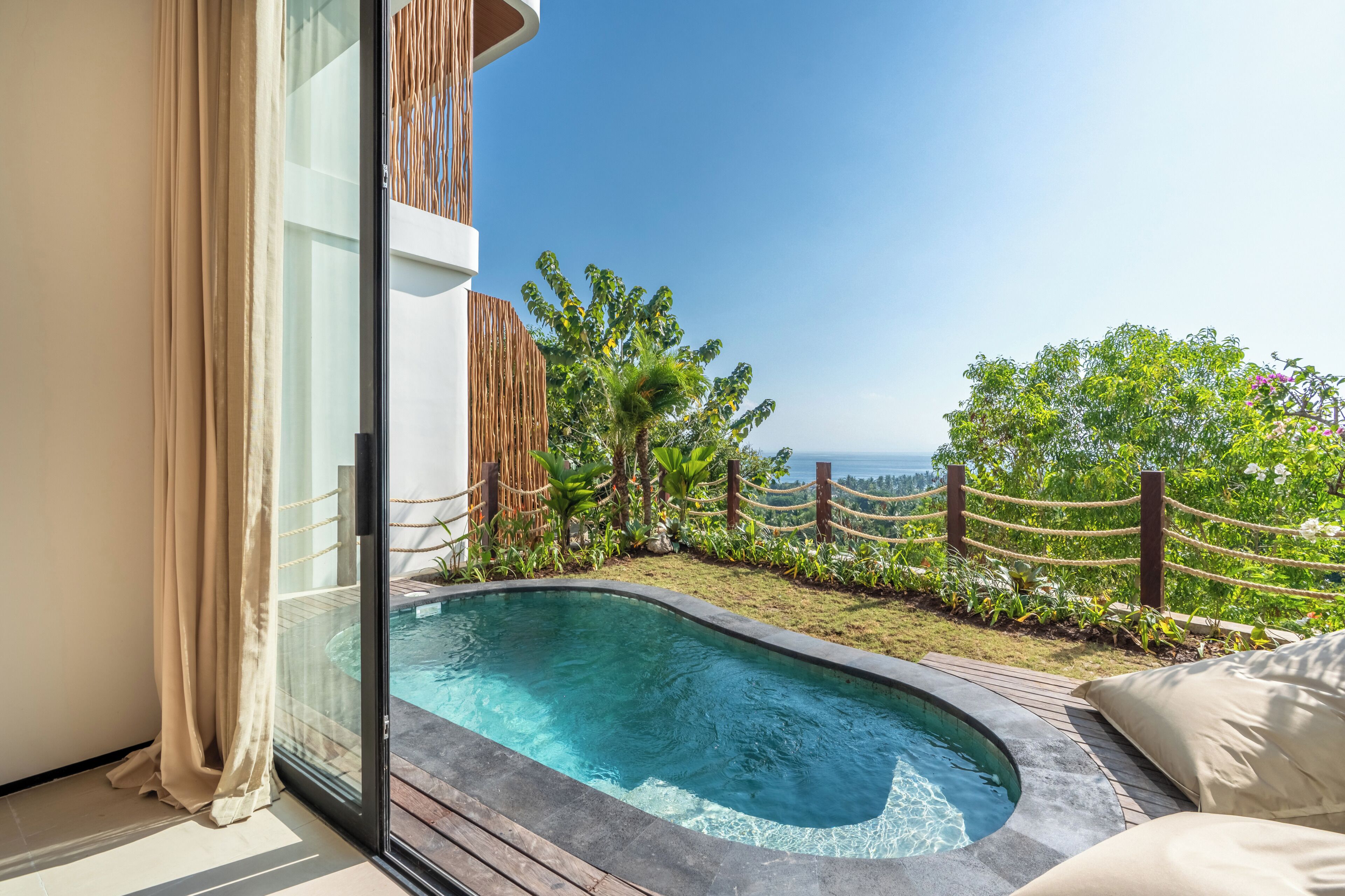 A modern outdoor pool area with a clear view of the ocean, surrounded by lush greenery and a wooden fence.