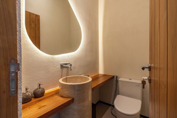 Un baño moderno con tocador de madera, lavamanos de mármol y un inodoro.