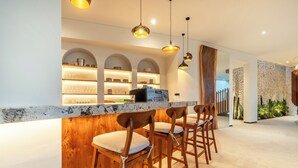 Una zona de bar con sillas de madera y una encimera de mármol, iluminación colgante y estantes con vasos y vajilla.