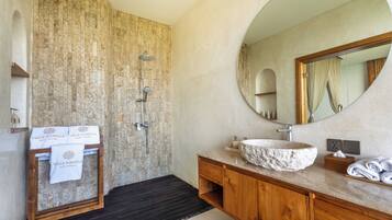 Une salle de bain avec un mur en pierre, un meuble-lavabo en bois, un miroir rond et une baignoire sur pieds.