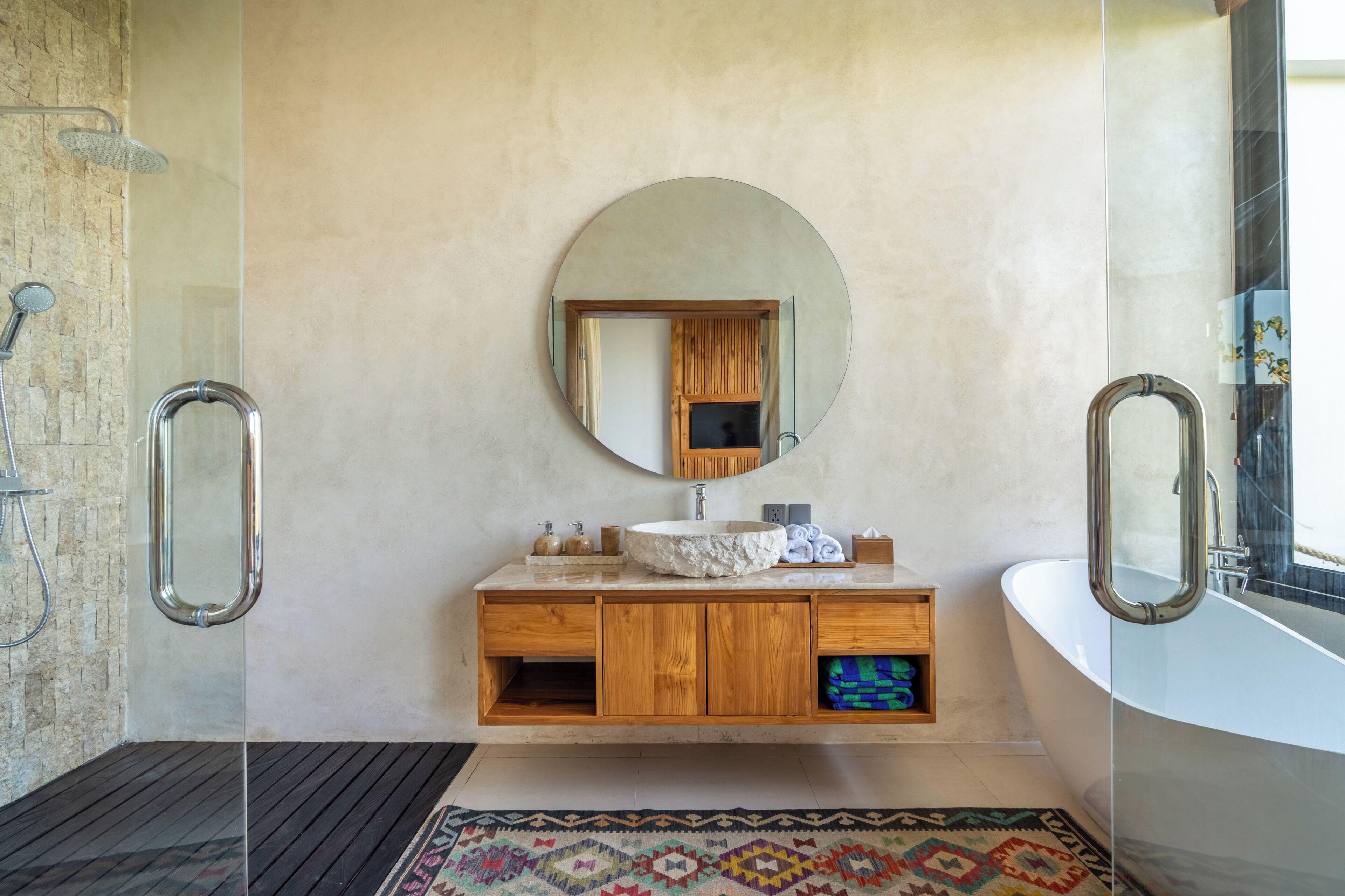 A modern bathroom with a stone sink, wooden vanity, a large mirror, and a glass shower enclosure.
