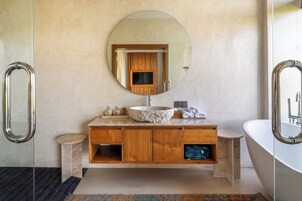 A modern bathroom with a round mirror, a stone sink, wooden cabinets, and a bathtub.