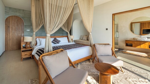 Un dormitorio moderno con una cama con dosel, una zona de estar con una mesita y un espejo grande.