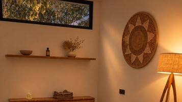 Un cuarto de spa con dos camillas de madera, un banco de madera, un estante montado en la pared con objetos decorativos y una lámpara de pie.