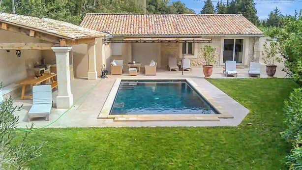 Ein Schwimmbecken mit Fliesen umgeben, mit Gartenmöbeln und einer überdachten Terrasse.