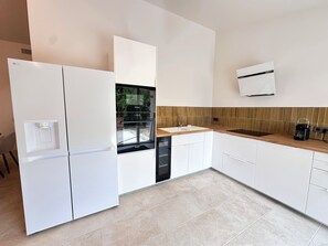 Uma cozinha moderna com armários brancos, uma geladeira Bosch, um forno Bosch, uma pia e uma cafeteira.