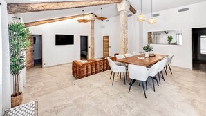 Ein modernes Interieur mit Essbereich, weißen Stühlen, einem Holztisch und einer großen Pflanze.