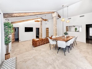 Interior moderno com área de jantar, cadeiras brancas, mesa de madeira e uma planta grande.