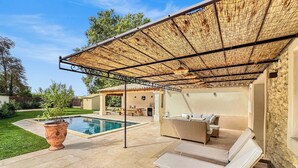 Ein überdachter Außenbereich mit Pool, Liegestühlen und einer Pergola.