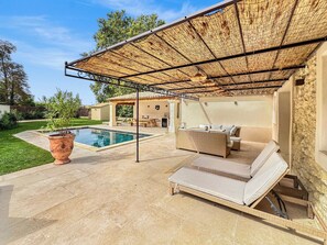 Uma área de estar coberta ao ar livre, com piscina, espreguiçadeiras e um pérgola.