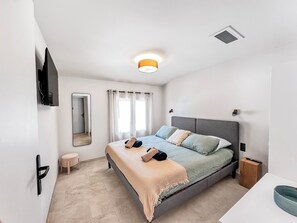 Quarto moderno com cama, mesa de cabeceira e televisão fixada na parede.