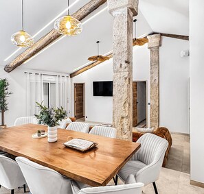 Een eetgedeelte met een houten tafel, witte stoelen en hangende lampen.