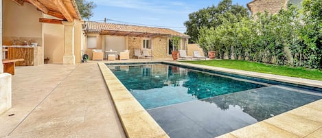 A swimming pool with a stone deck, outdoor seating, and a stone building in the background.
