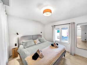 Un dormitorio moderno con cama, mesita de noche, ventana con cortinas e iluminación en el techo.