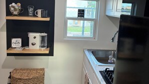 Ett kök med vita skåp, en diskho i rostfritt stål, en mikrovågsugn och en inredning med kaffetema, inklusive en griffeltavla med ord och uttryck som har med kaffe att göra.