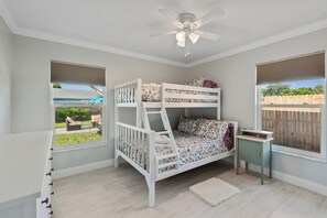 Ein Schlafzimmer mit Etagenbett, Deckenventilator, Fenster mit Blick ins Freie und einem kleinen Nachttisch.