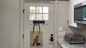 A kitchen with a white door, a window, an air conditioner, a microwave, and a countertop. - Equestrian cottage— country living in the city (Aiken)