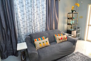 A grey sofa with two decorative pillows, a white side table, a black metal shelf with decorative items, and a patterned rug. - 2-bedroom apartment in fantastic Montego Bay with AC (Montego Bay)