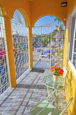 Ein Balkon mit gelben Wänden, einem Glastisch, einem Stuhl und einem Blumentopf mit Blumen.