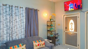 A living room with a grey sofa, colorful cushions, a television mounted on the wall, a small shelf with decorative items, and a door with a frosted glass window. - 2-bedroom apartment in fantastic Montego Bay with AC (Montego Bay)