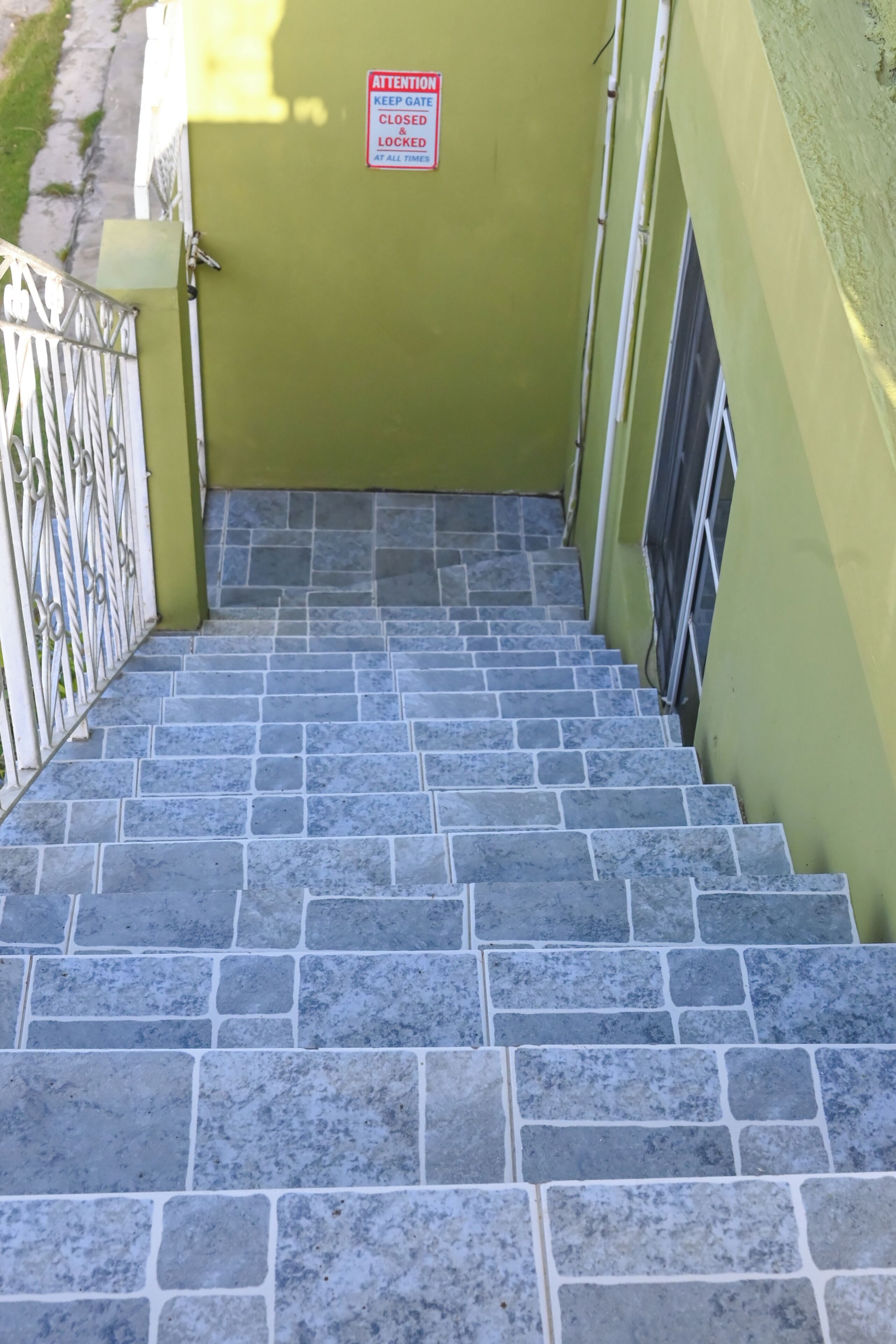 A set of stone stairs leading to a green door with a sign that reads 'ATTENTION KEEP GATE CLOSED & LOCKED AT ALL TIMES.'