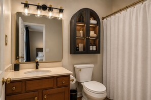 Un baño con tocador, inodoro, espejo con iluminación y mueble de almacenamiento para artículos de aseo.