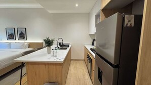 A compact hotel room with a kitchenette, a bed, a bedside table with a plant, and framed pictures on the wall. - w* | Enchanting Loft in the Heart of Roma Sur (Ciudad de México)