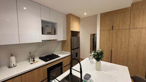A modern kitchen with white cabinets, a stainless steel refrigerator, and a dining area with a white table. - w* | Enchanting Loft in Roma Sur (Ciudad de México)