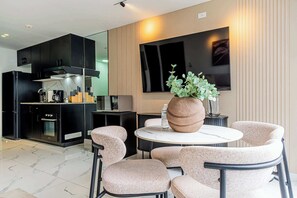Eine moderne Küche mit schwarzen Schränken, einem eingebauten Backofen und einer Mikrowelle. Ein runder Esstisch mit vier Stühlen, eine große Vase mit Grünpflanzen und ein Flachbildfernseher an der Wand.