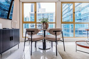 Ein modernes Interieur mit Essbereich, inklusive rundem Tisch, vier Stühlen, einer Topfpflanze und Blick auf eine Stadtlandschaft durch große Fenster.