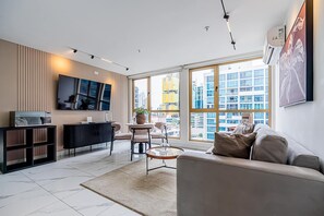 Ein modernes Wohnzimmer mit Sofa, Couchtisch, Fernseher und einem großen Fenster mit Blick auf die Stadt.