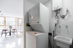 Ett kompakt tvättrum med en inbyggd tvättmaskin och torktumlare, ett litet handfat och ett fönster med utsikt över byggnader.